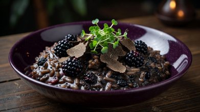 Creamy dark truffle and blackberry risotto served in a deep purple ceramic bowl with microgreens and shaved black truffle